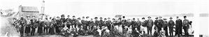 Long rows of men and women pose for the camera along a bay with a barn in the background